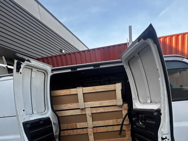 White van with its rear doors open, loaded with crated goods